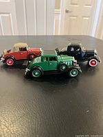 Set of three vintage toy cars grouped together on a black surface showing different colors and styles.