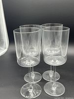 Four clear cylindrical wine glasses with straight walls and thin stems and round bases, shown on black background.