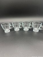 Four clear glass espresso cups lined up side by side on a black background.