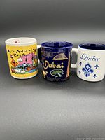 Front view of New Zealand, Dubai, and Quebec espresso cups showing colorful and text designs