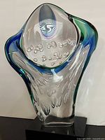 Front view of clear glass sculpture with blue and green accents and bubble inclusions on black base.