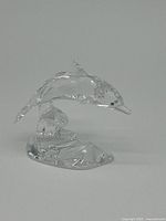 Clear crystal dolphin figurine on a wave-shaped base set against a plain background