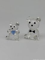 Front view of two miniature Swarovski crystal bears, one larger with bow tie, one smaller with blue heart