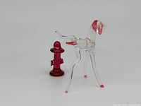 Clear crystal dog figurine with red accents and red crystal fire hydrant figurine shown side by side on a plain background.
