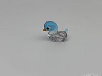 Photo showing front-facing view of the Swarovski miniature blue-headed duck crystal figurine with blue head and orange beak on a plain background.