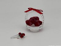 Photo showing clear and red crystal heart basket with a red bow and three red hearts inside, accompanied by a small rose bouquet with red flowers and green leaves on a clear cone base.