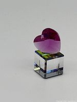 Front and side view of a Swarovski miniature pink faceted heart crystal mounted on a clear crystal cube base, showing the color gradient and the faceting details.
