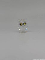 Front view of the clear crystal owl figurine showing jewel yellow eyes and faceted design, standing on a small base.