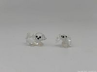 Two Swarovski miniature puppy figurines made of clear faceted crystal with black eyes, shown side by side on white background