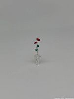 Clear view of Swarovski miniature roses with two red flowers and green leaves in a small crystal vase