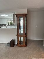 Front and side view of the tall narrow wooden curio cabinet showing the curved glass panels and overall shape.