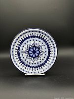 Full view of round Talavera clay plate with white background and dark blue intricate floral and geometric patterns.