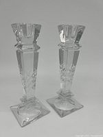 Pair of clear crystal pillar candlestick holders with geometric cut detailing and square bases.