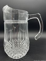 Side view of clear glass pitcher with detailed cut glass Longchamp pattern on bottom, smooth spouted top and faceted handle