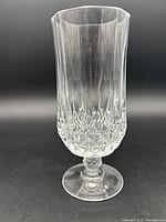 Single vintage Cristal d’Arques Longchamp crystal footed glass with faceted cut design shown against black background.