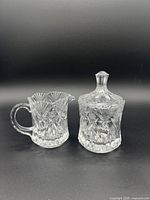Photo of the creamer and sugar bowl with lid together against black background.