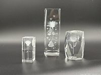 Photo showing three vintage laser etched glass paperweights with rose designs on a dark background.