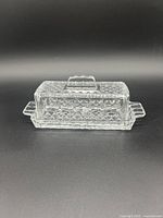 Front view of butter dish with lid on showcasing the cut-glass diamond and starburst pattern and side handles.