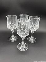 Front group view of 4 clear crystal Longchamps Cristal d’Arques stemmed wine glasses showing intricate cut pattern and clear bases.