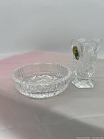 Photo showing the Waterford crystal ashtray and toothpick holder on a white surface with a pink background, displaying the crystal's cut design and Waterford labels.