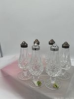 Set of six Waterford Crystal Lismore footed salt and pepper shakers displayed on a pink cloth background, showing two sets with distinctive metal lids and clear cut crystal bodies.