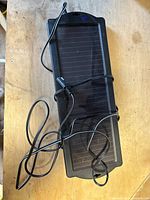 Top view of black rectangular solar panel charger with attached cable, placed on wooden surface.