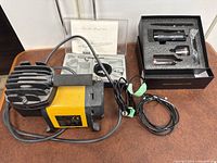 Mini air compressor with yellow housing accompanied by accessories box and airbrush case