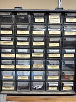 Workshop organizer showing multiple labeled drawers containing 5/64 machine screws, machine screws with various thread sizes, mute pads, washers including drip washer and flat washer, wood screws, plastic putty, rubber grommets, and other small hardware items.