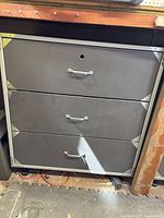 Closed metal cabinet with three drawers and metal corner reinforcements.