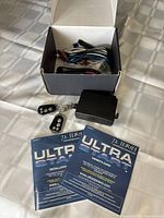 Overview of box with wiring, black module, two remote key fobs, and two manuals laid out on table.