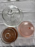 Top view of three covered glass cake dishes: clear large one, pink embossed smaller one, and brown glass one.