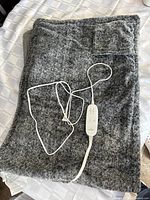 Folded gray electric blanket showing texture and attached white remote control with buttons.