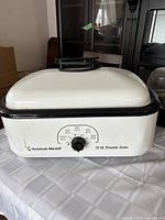 Front view of the white American Harvest electric roaster oven with black trim and control knob on a white checkered tablecloth.