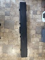 Closed black rectangular firearm case on tile floor, showing the exterior shape and size.