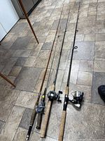 Lot showing four fishing rods with attached reels laid out on tiled floor.