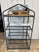 Full view of the greenhouse frame with wire mesh shelves, grow light, plastic cover wrapped and cardboard box on top.