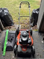 Front view showing mower, folded handle, grass catcher bag and accessories