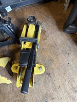 Yellow hydraulic floor jack with black handle shown on wooden floor.