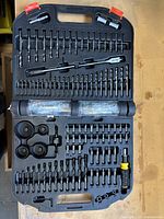 Opened drill bit set case showing all included drill and driver bits, hole saws, extensions in molded black case with red clasps.