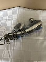 Electric personal massager laying on white cloth, showing full unit with cord and handle.