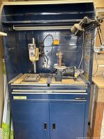 Blue Mastercraft cabinet with pegboard hutch, ShopCraft drill press on left and bench belt/disc sander on right