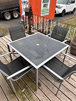 Patio table and four chairs arranged on wood deck, showing top angle of the table and chairs.
