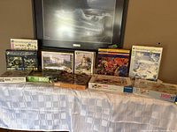 Assorted puzzle boxes displayed on a table showing a variety of puzzles mostly 1000 pieces including Ravensburger and other brands.