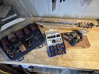 Overview of rotary tool accessories on workbench including sanding bands, grinding bits, polishing stones, and rotary tool parts.