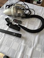 Full view of Euro-Pro Shark handheld vacuum with black hose and multiple attachments including brush, crevice tool, and nozzle.