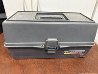 Closed gray Woodstream plastic tackle box with handle and latch on table.