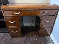 Front view of wooden desk showing six drawers and decorative carved wood detail.