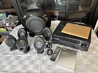 Full view of Yamaha home theatre components including the subwoofer, five satellite speakers, AV receiver, remote, manual, and two speaker stands laid out on a table