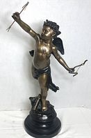 Front and side view of the bronze cherub figurine standing on a black round base, holding a bow and three arrows, showing detailed features and antique finish.