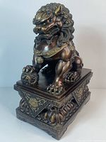 Full view front-right of bronze Fu dog seated on a square pedestal with ornate base.